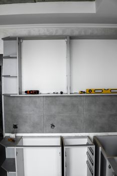 Custom kitchen cabinets installation without a furniture facades mdf. Gray modular kitchen from chipboard material on a various stages of installation in kitchen with a grey tile on floor and walls