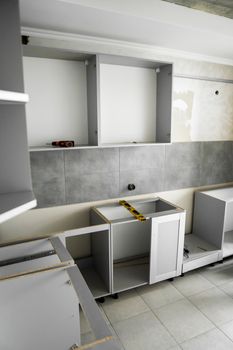 Custom kitchen cabinets installation without a furniture facades mdf. Gray modular kitchen from chipboard material on a various stages of installation in kitchen with a grey tile on floor and walls