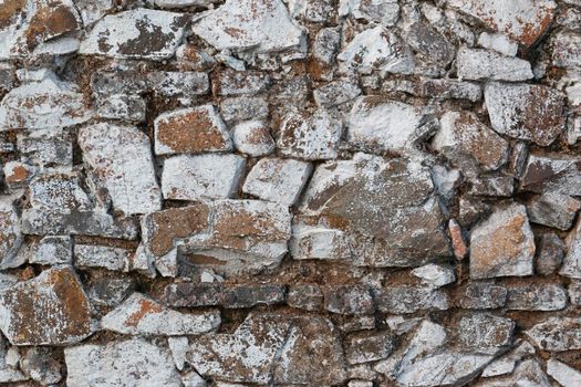 Old stone wall, painted in a faded white color and built with stones and mud