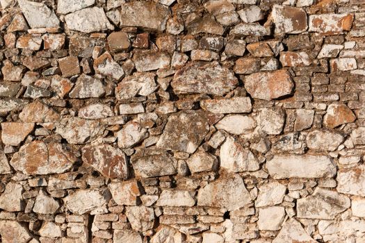 Old stone wall, painted in a faded white color and built with stones and mud