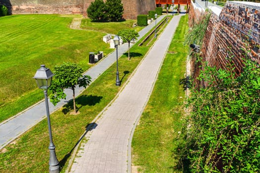 Green garden with clean grass, beautiful trees, alleys in a fortress yard. The fortification walls and promenades in Alba Iulia, Romania, 2021