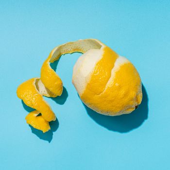 Lemon with spiral peeled zest over blue minimalistic background. Lemon and peel in hard light. Top view or flat lay. Summer minimalistic creative concept and layout. Square