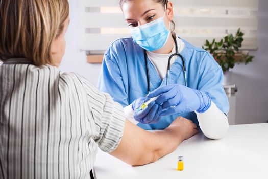 Young female doctor vaccinating elderly patient in UK GP's office,virus disease therapy and treatment,remedy and cure for infections or seasonal flu,Coronavirus COVID-19 potential vaccine development