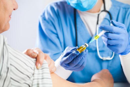 Female GP doctor holding ampoule vial with yellow liquid,filling syringe with injection shot,vaccinating elderly patient,Coronavirus COVID-19 virus disease immunization concept,vaccine clinical trial