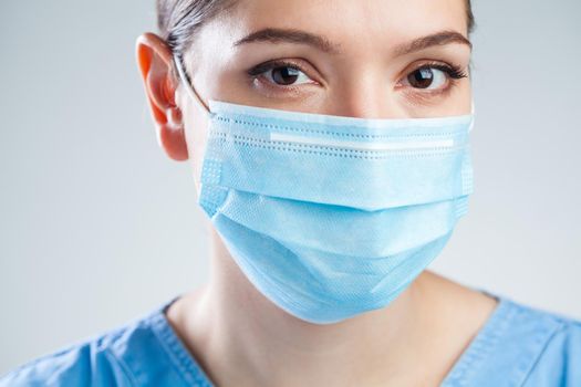Portrait of young beautiful female EMS medical worker,wearing blue uniform and protective face mask,studio headshot isolated on white background,stress and worry due to Coronavirus COVID-19 pandemic