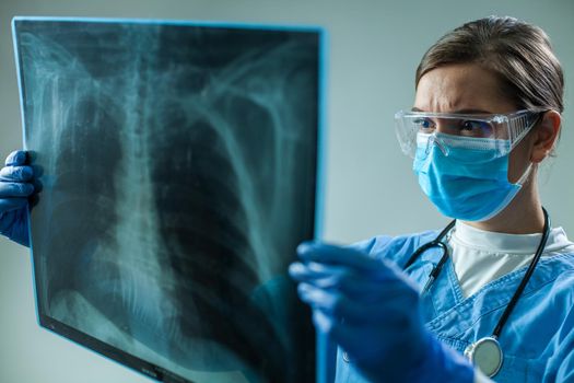 Female GP doctor holding chest x-ray film scan,medical woman worker examining patient lungs during Coronavirus severe acute respiratory disease pandemic crisis,wearing PPE,gloves,face mask & goggles