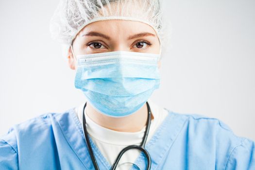 Concerned caucasian UK NHS doctor isolated on white background portrait,wearing medical PPE Personal Protective Equipment,face mask & hair cover,serious troubled look in eyes,worried stressed & tired