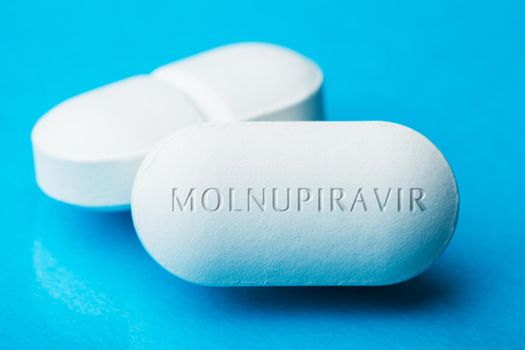 COVID-19 experimental antiviral drug MOLNUPIRAVIR,two white pills with letters engraved on side,potential experimental WHO Coronavirus cure,pandemic outbreak crisis,isolated on blue background