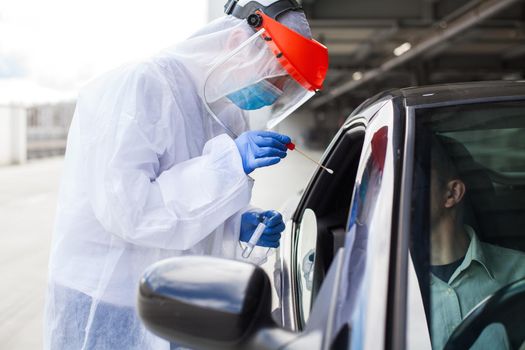 Medical worker in PPE performing nasal & throat swab on person in vehicle through car window,COVID-19 mobile testing centre,drive through facility parking lot,specimen collection and rt-PCR diagnostic