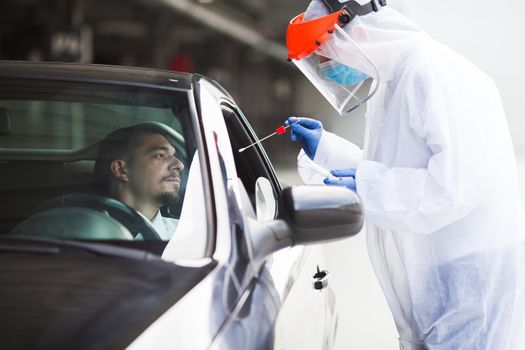 COVID-19 drive-thru rt-PCR detection site,medical worker performing nasal swab specimen collection on young male driver,free Coronavirus public diagnostic procedure,mobile car testing center clinic