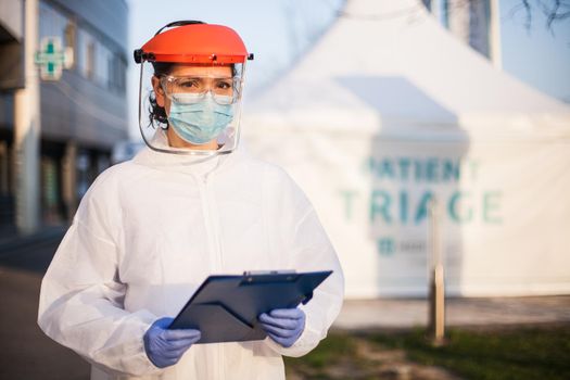 Worried exhausted and stressed frontline UK NHS doctor,wearing PPE & face shield,out of hospital patient triage tent quarantine,special US COVID-19 intensive care unit facility for close contact cases