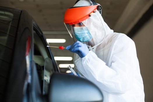 Medical worker in personal protective equipment swabbing a person in a car drive through Coronavirus COVID-19 mobile testing center,oral and nasal specimen collection procedure,health and safety