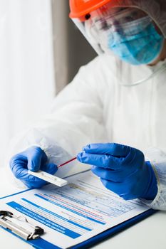 Lab technician medical scientist performing Coronavirus COVID-19 rapid diagnostic testing for antibodies, wearing personal protective equipment PPE, placing blood sample specimen on test using pipette