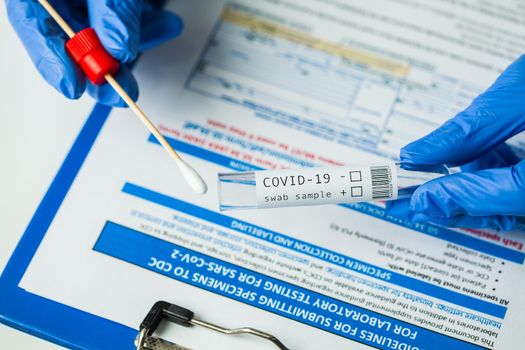 Medical worker holding swab sample collection kit,test tube for performing patient nasal swabbing,hand in gloves holding testing equipment over specimen submitting form,Coronavirus COVID-19 diagnostic