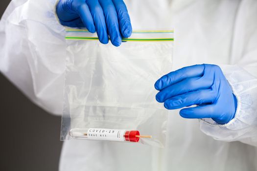 Coronavirus COVID-19 self swab collection kit,scientist in blue surgical gloves and white protective suit holding specimen testing equipment in a transparent bag,PCR nasal and oral sample test tube