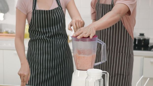 Happy young family couple husband and wife making fresh apple smoothie in kitchen together. The man and woman help each blender the apples with a juice blender. Healthy lifestyle concept,