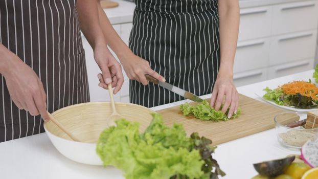 Happy Asian beautiful family couple husband and wife cooking vegetable salad in kitchen together at home. The man mix the vegetables in a cup woman cut vegetables. healthy food concept