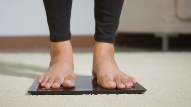 Asian young woman leg stepping standing on floor electric scales, female working out at home in living room, female stand on digital weighing machine. Healthy weight loss control concept, slow motion