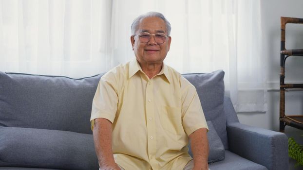 Head shot portrait old man grandfather smile with eyeglasses relaxing looking at camera, Asian happy senior old gray-haired sitting in the living room on sofa alone at home, older people health care
