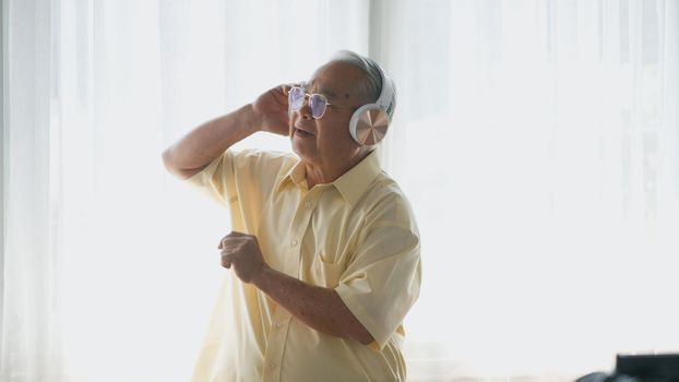 Asian elderly man or grandpa, happy senior retired guy with headphones listening music radio and moving dancing enjoying every moment of his funny life