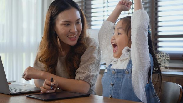 Asian young mother working with laptop computer at home and help daughter doing homework, Single mom freelancer work from home and helping his girl kid teaching homework on desk