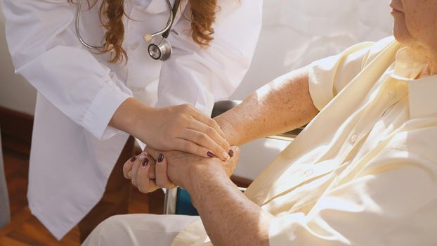 Female nurse doctor wear white uniform holding hand of patient senior or elderly old man during sit on wheelchair encourage empathy at nursing hospital, older people healthcare support