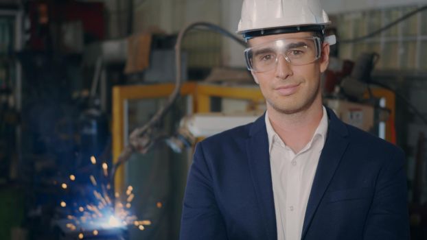 Professional confident engineer businessman in suits safety hats, goggles smile look at camera stand in heavy industrial facility manufacturing with steel welding from with fire spark