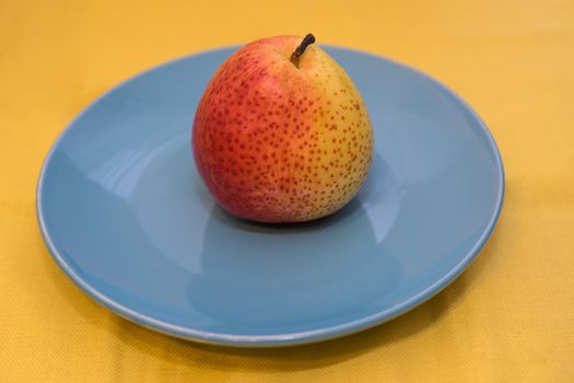 Juicy and bright pear on blue ceramic plate standing on a yellow tablecloth