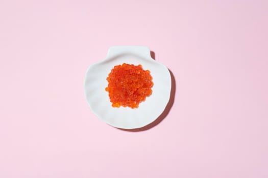 Porcelain plate with red caviar on a pink background.