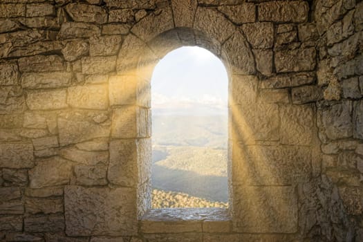A window in a stone wall overlooking a mountain landscape.