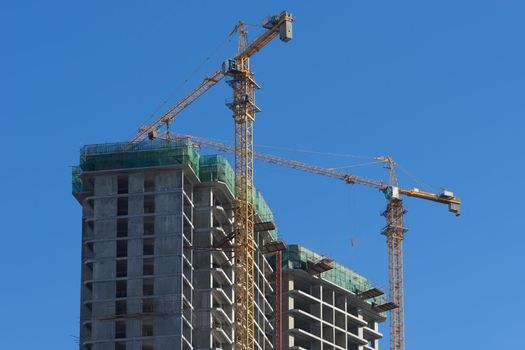 Urban landscape with views of the house under construction and cranes against the blue sky.