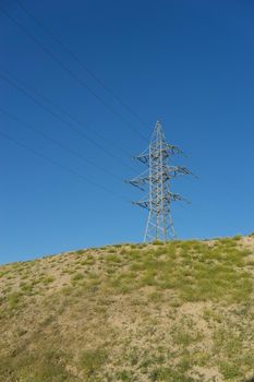 electric tower with wires on the hill against the blue sky.