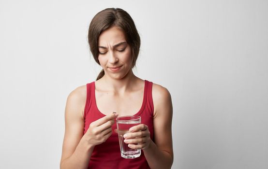 makeup woman in red t-shirt holds glass of water pill medicine health problems. High quality photo
