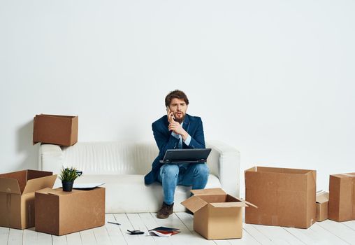 A man sits on the couch in front of a laptop working boxes with things unpacking a new office. High quality photo