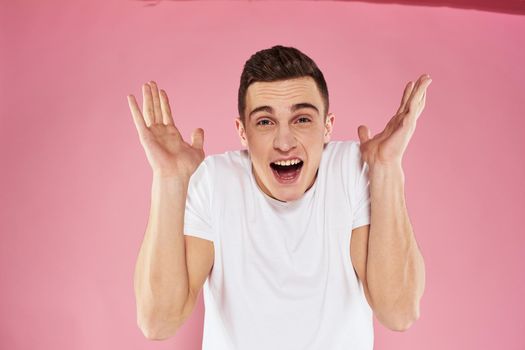 A man in a white t-shirt gestures with his hands emotions pink background studio cropped view. High quality photo