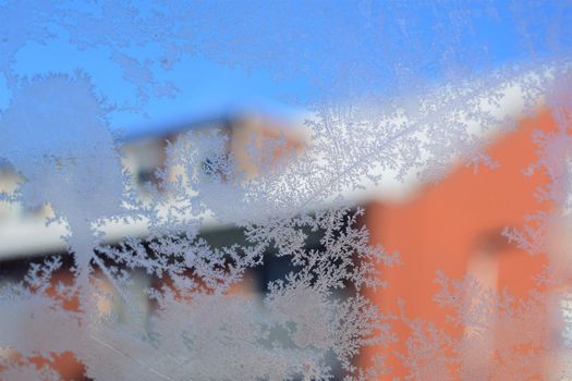 Texture as a frosty pattern on a window glass as a close-up with a red house inthe background