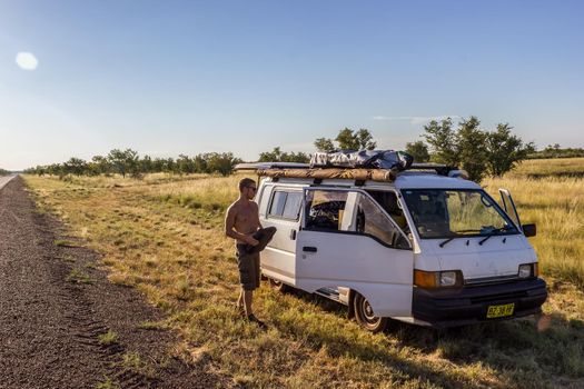 young caucasian man with tool kit in his hands is walking around his van next to a outback road after car break down, Western Australia.