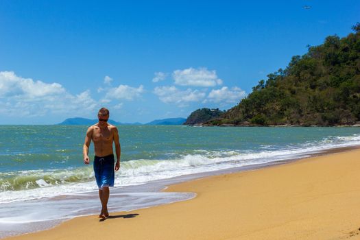 Muscular Hawaiian man walking on the beach as ocean waves crash behind him