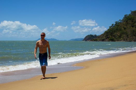 Muscular Hawaiian man walking on the beach as ocean waves crash behind him