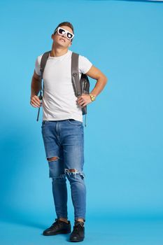 Cheerful young guy with backpack studio blue background. High quality photo