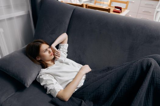 a woman in a white t-shirt lies on the sofa under a blanket. High quality photo