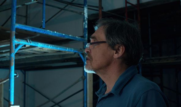 Elderly male architect at a construction site. He looks at something and talking. Close up portrait