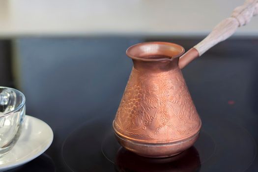 A copper turk for brewing coffee stands on a glass-ceramic plate. Make coffee in a turk. Aromatic coffee. 