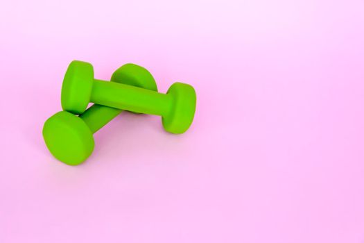 Green dumbbells for sports on a pink background. Sports, sports nutrition, healthy eating, diet. Space for the text. Exercise, lose weight.