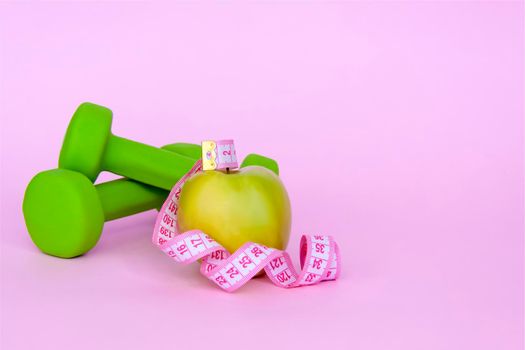 A green apple, and a centimeter measuring tape on a pink background. Sports, sports nutrition, healthy eating, diet. Space for the text. Exercise, lose weight 