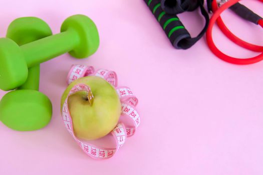 A green apple, and a centimeter measuring tape on a pink background. Sports, sports nutrition, healthy eating, diet. Space for the text. Exercise, lose weight 