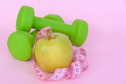 A green apple, and a centimeter measuring tape on a pink background. Sports, sports nutrition, healthy eating, diet. Space for the text. Exercise, lose weight