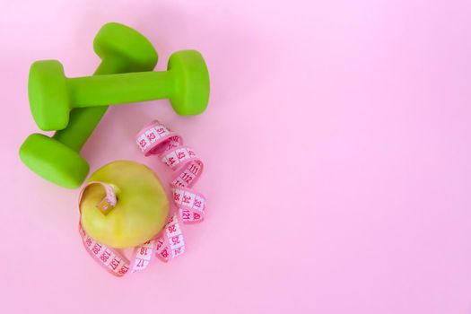 A green apple, and a centimeter measuring tape on a pink background. Sports, sports nutrition, healthy eating, diet. Space for the text. Exercise, lose weight