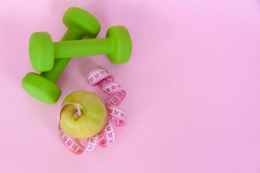 A green apple, and a centimeter measuring tape on a pink background. Sports, sports nutrition, healthy eating, diet. Space for the text. Exercise, lose weight