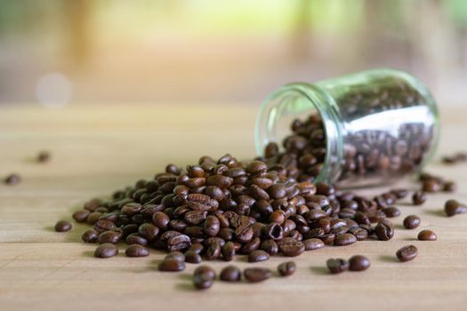 Roasted coffee beans in glass bottles placed on the table with nature background.